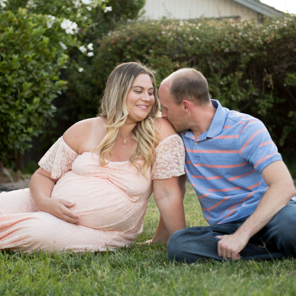 man kissing pregnant woman on should wearing a pink dress